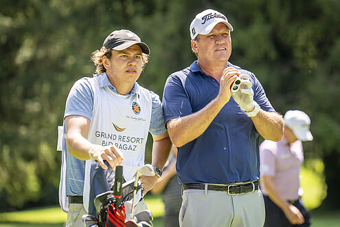 Jarmo Sandelin und sein Sohn (sein Caddy) stehen auf dem Golfplatz, der eine hält die Schläger in, der andere im blauen Hemd ist sehr konzentriert. Ein heller, sonniger Tag.
